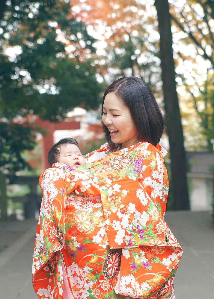 世田谷八幡宮でのお宮参りでオレンジ色の祝い着を掛けるママ