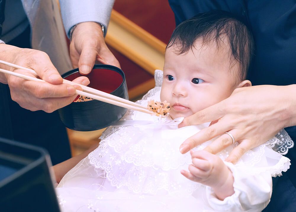 お食い初めお膳の赤飯を食べようとする赤ちゃん