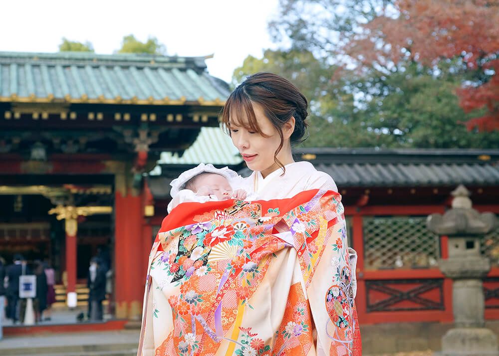 根津神社でお宮参りでオレンジ色の祝い着・産着（着物）をかけたママ