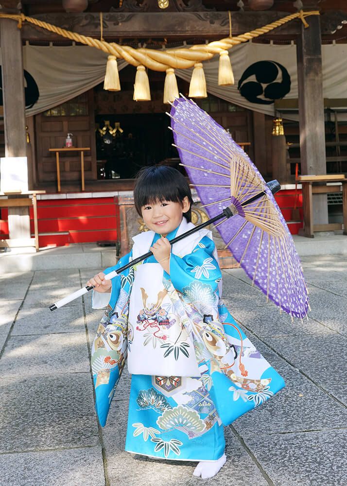 草加神社の本殿前で紫色の和傘を持ってポーズをとる3歳男の子