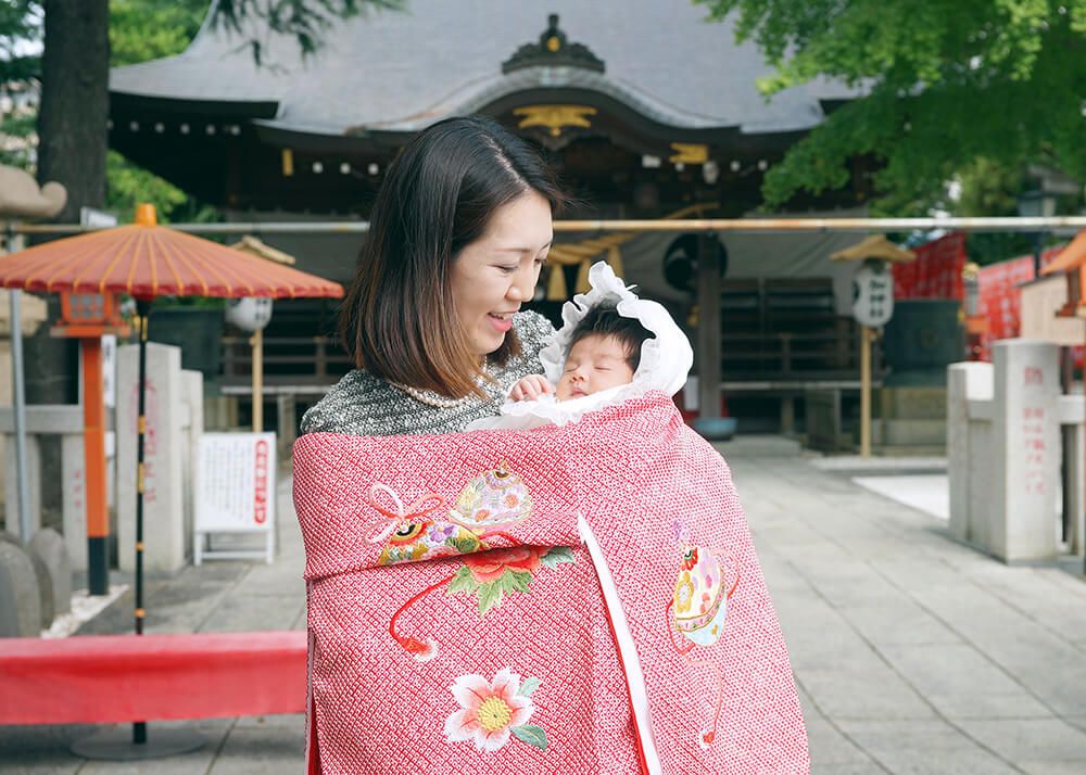 草加神社でのお宮参りで赤い色の祝い着をかけるママ