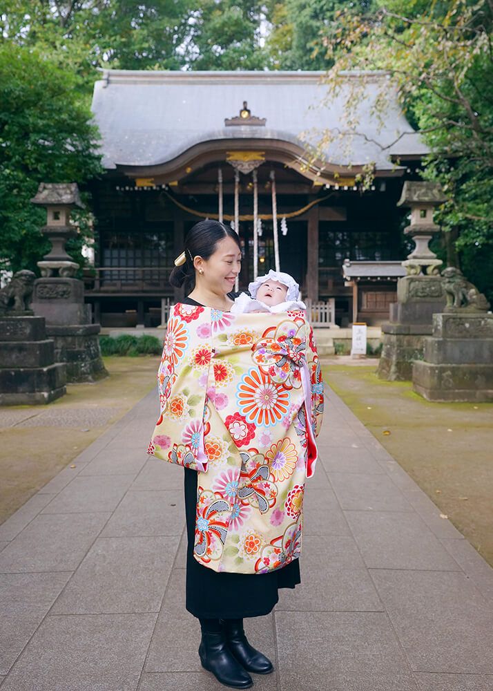 石神井氷川神社の本殿前でお宮参りの祝い着をかけたママ